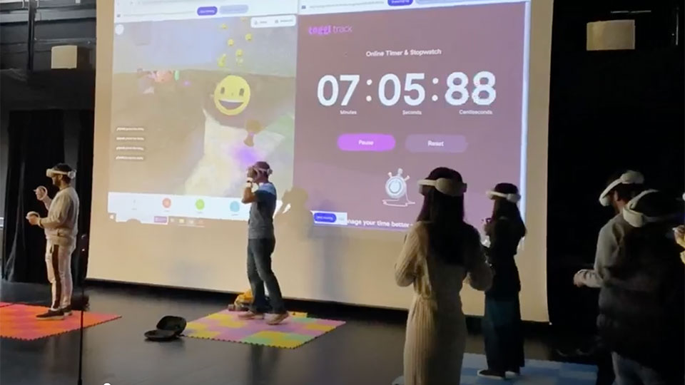Students in a large room wearing VR headsets with a projection screen in the background