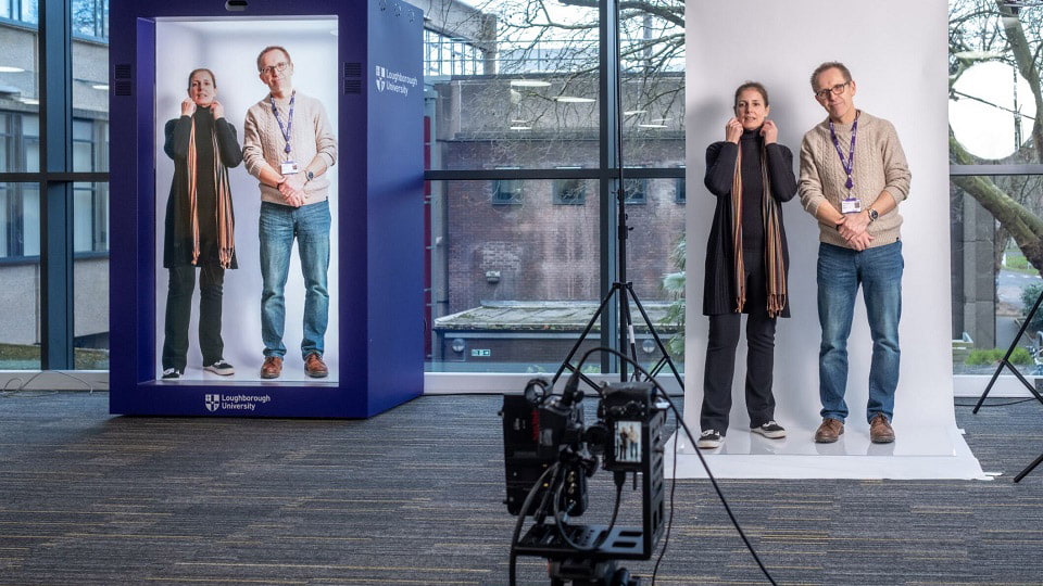 Two members of staff being filmed and appearing on the hologram screen next to them.