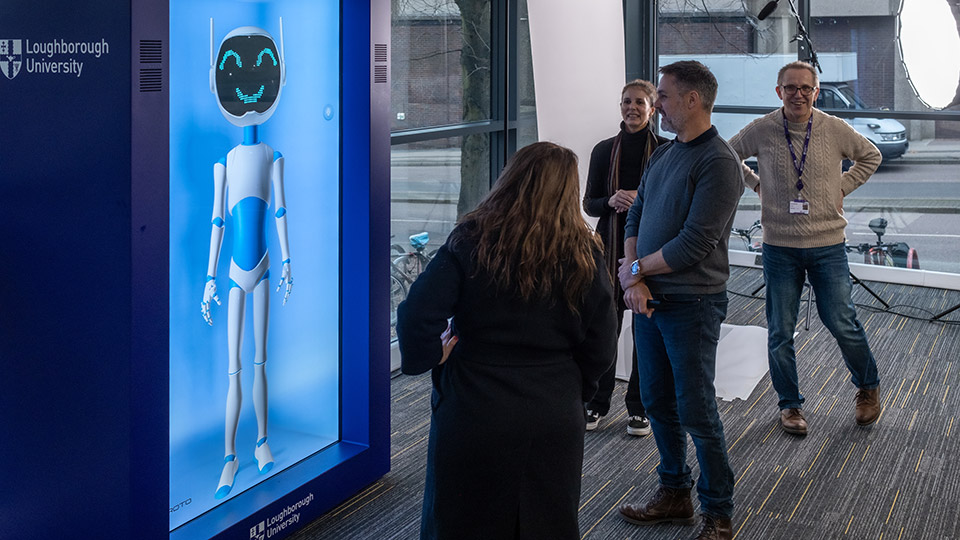Members of staff stood looking at the Proto hologram box and AI bot.