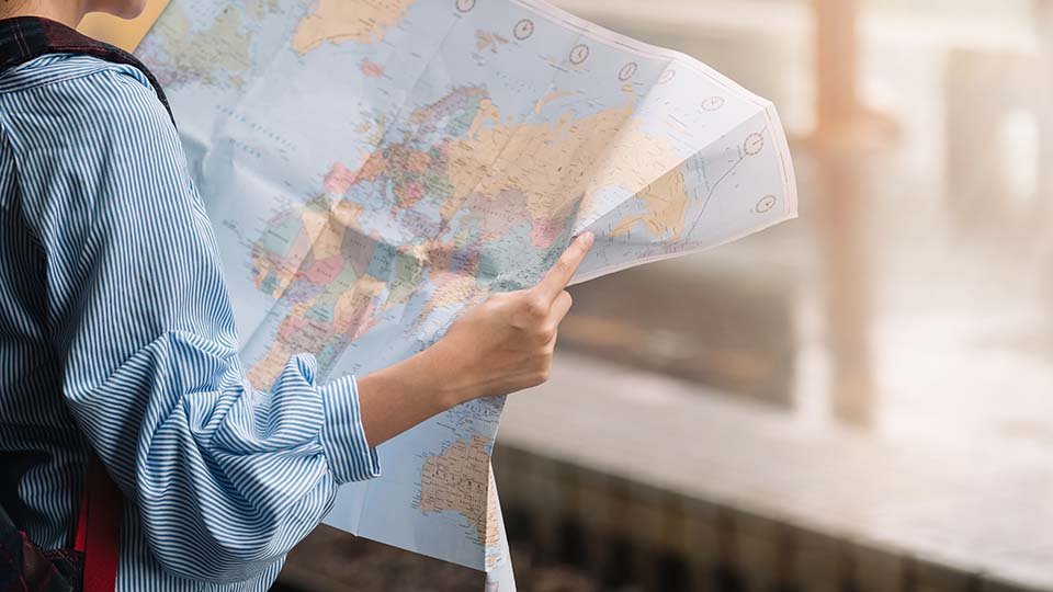 Young person holding a map of Europe, pondering their next move, maybe? Free image licensed from Adobe Stock.