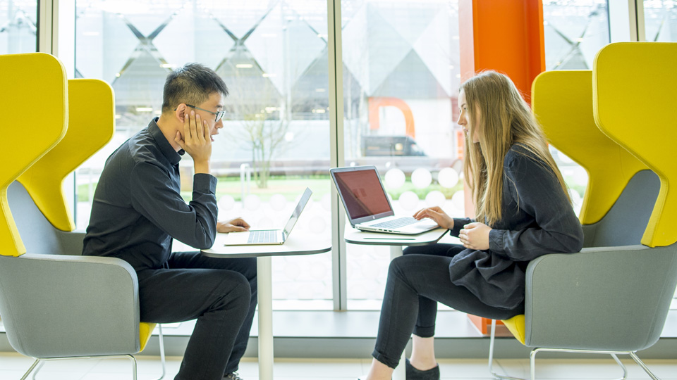 two students sitting opposite each other using laptops