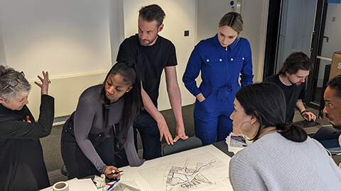 Students standing around a table with an industry professional showing them architectural designs.