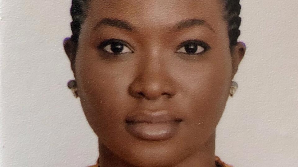 Female student smiling at the camera in front of a white background, wearing gold earrings.