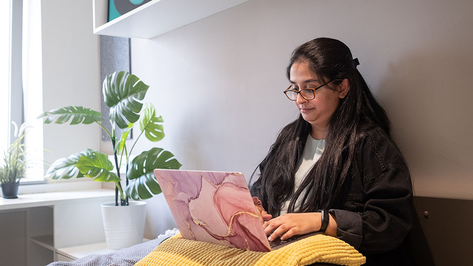Student working on laptop in her room in London private halls