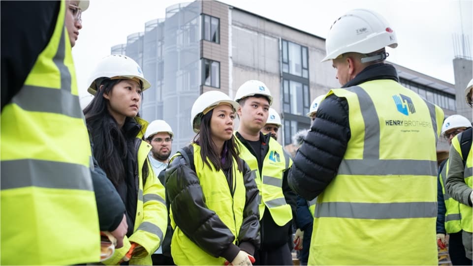 Students at a building site wearing hard hats and high visibility jackets
