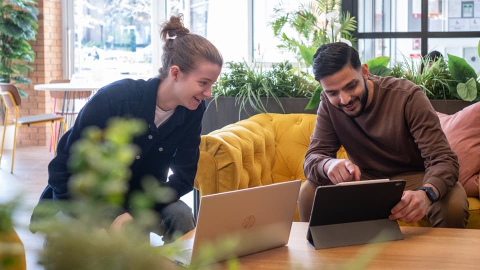 Two students in a cafe looking at their laptop computers