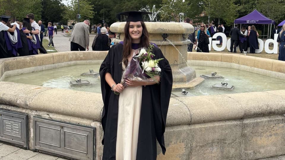 MSc Work Psychology student, Annie McCarron standing in front of a fountain at her Loughborough University undergraduate graduation ceremony.