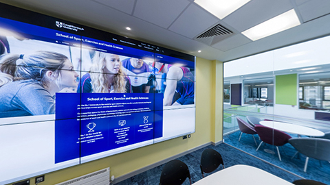 A room with a large screen, tables and chair for collaborative work