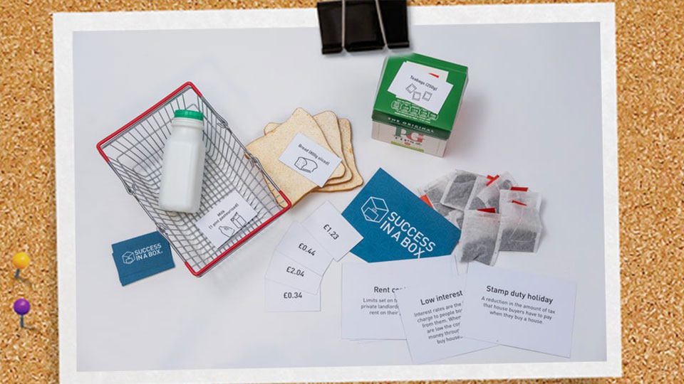 A selection of items including bread,a teabag box, bottle of milk, food baskets and card activities.