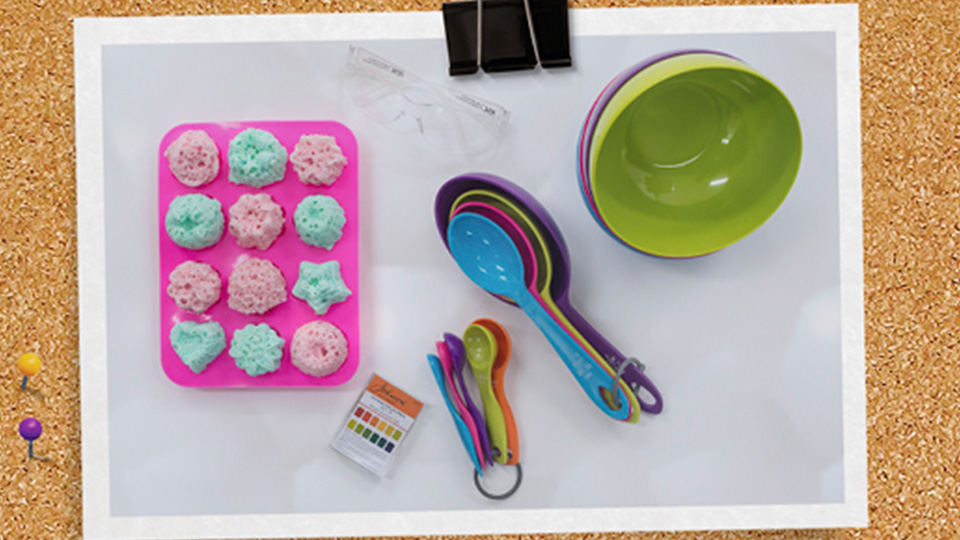 Equipment including bath bombs inside a mould, measuring spoons and a bowl.