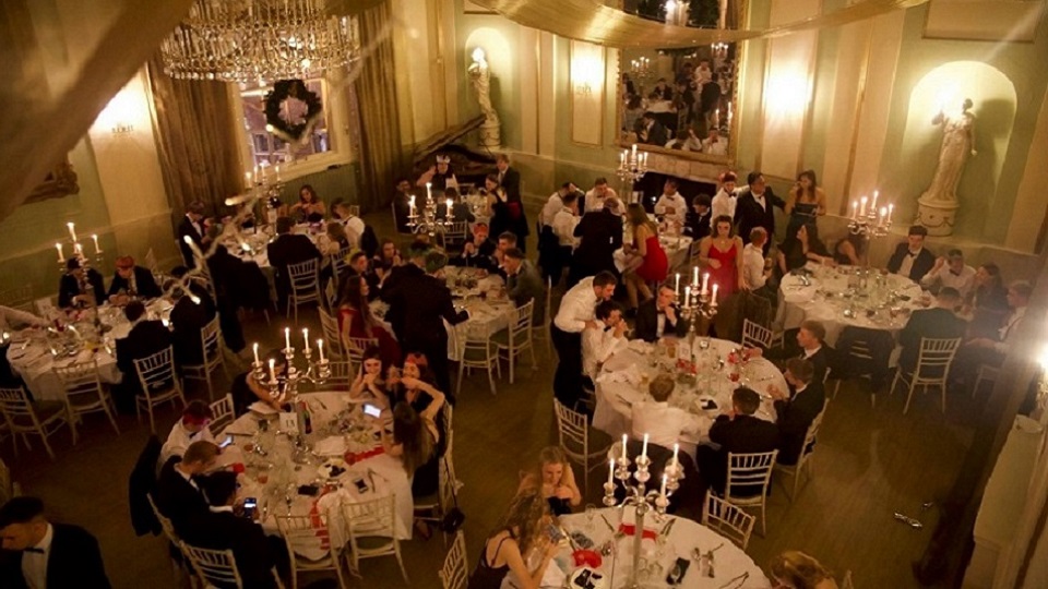 An overhead image of students sitting at tables at a university hall ball event.