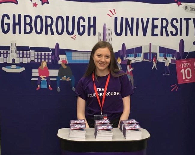 Photo of Eleanor in front of a Loughborough University banner during her placement year.