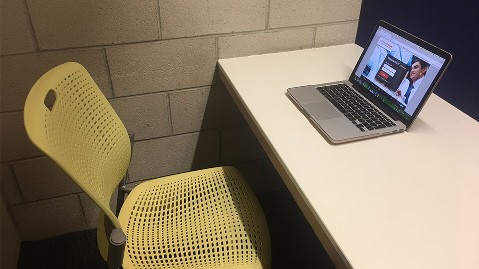 A desk with a laptop on the top and a chair underneath.