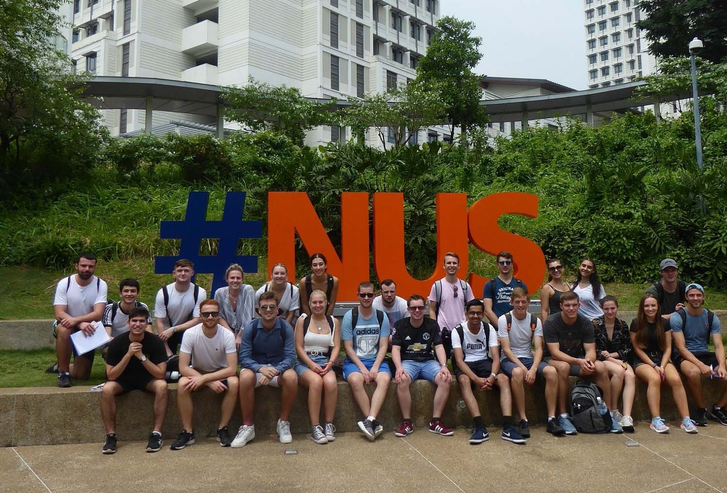 Joe and other students during a field trip sitting in front of a #NUS sign.