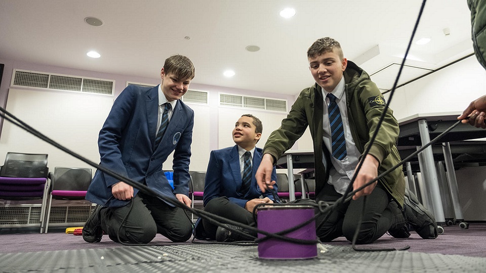 three male pupils and a lecturer setting up an experiment