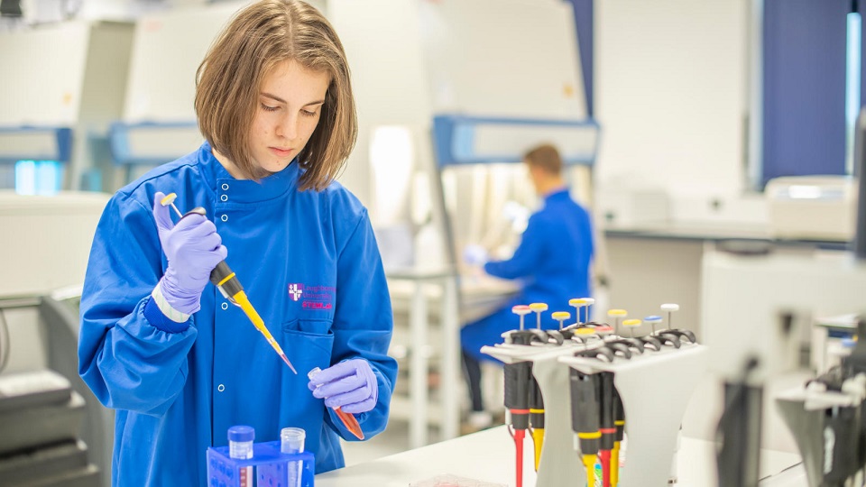 A female student pipetting in the STEMLab bio projects lab while a fellow student works in the background.