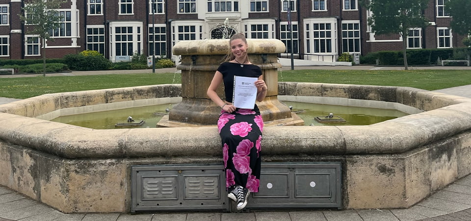 Lily sits by a fountain, holding a piece of paper.