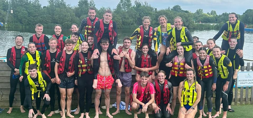Rufus with a big group of friends stood together next to some water