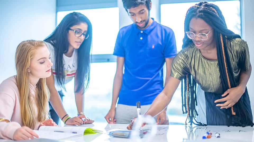 Four students standing over a desk writing on sheets of paper