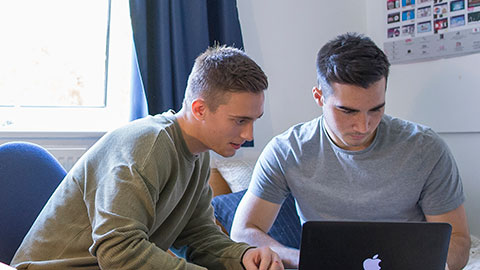 Two male students looking at a laptop computer in a student bedroom