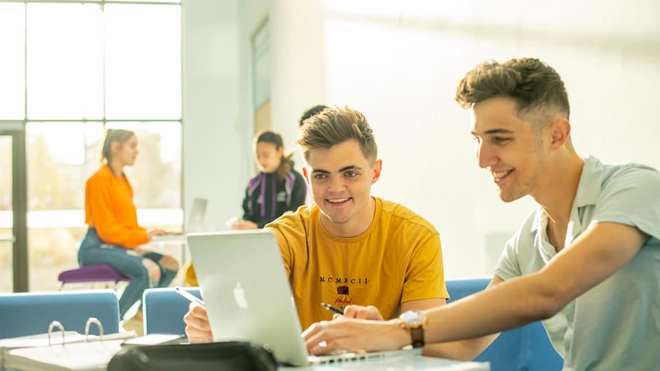 Students sat at a table looking at a laptop screen.