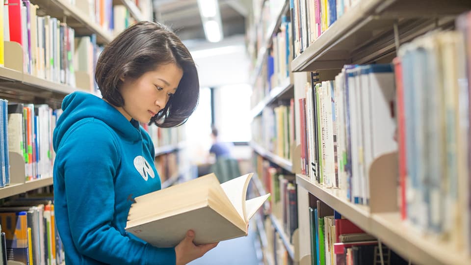 A student stood reading a book in the Library.