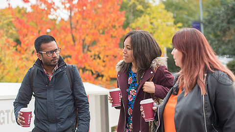 Three mature students holding cups of coffee walking into the Library