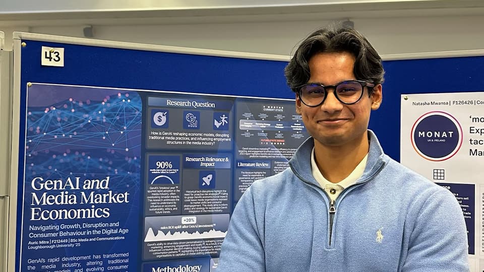 Headshot of Auric smiling to camera with work poster in the background