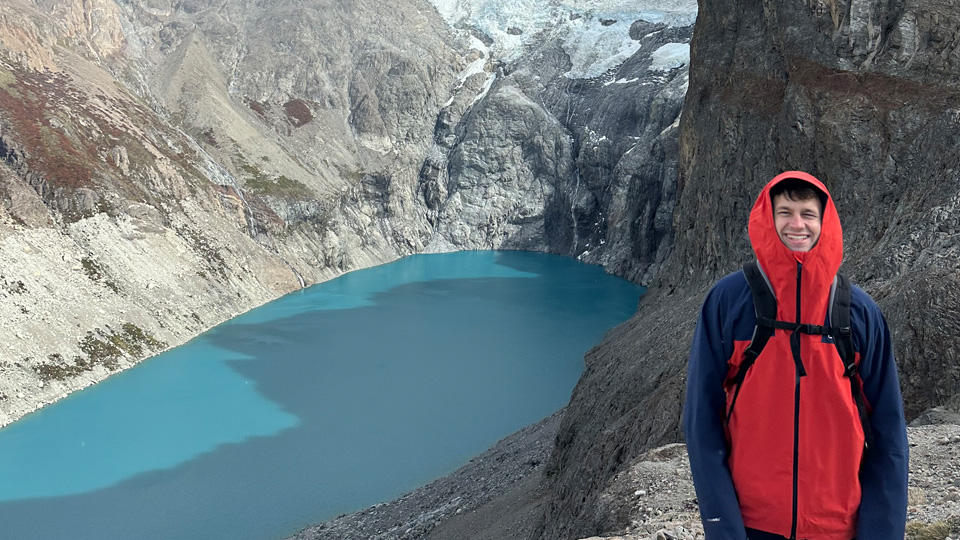 Student Luke Lewis poses in front of a mountain lake.