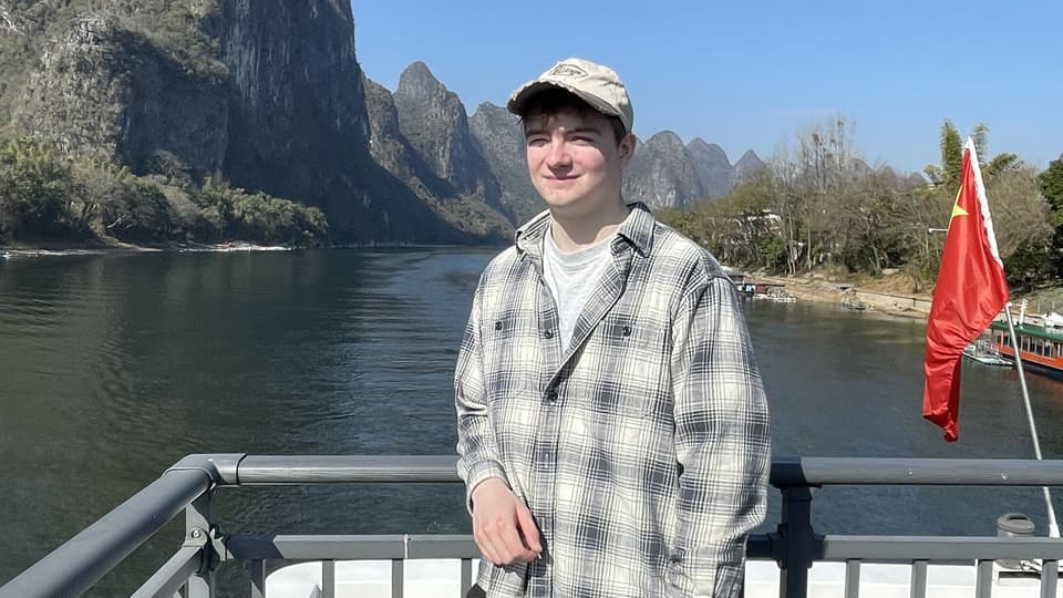 BSc Economics student Oscar Baker.stands at the front of a riverboat.