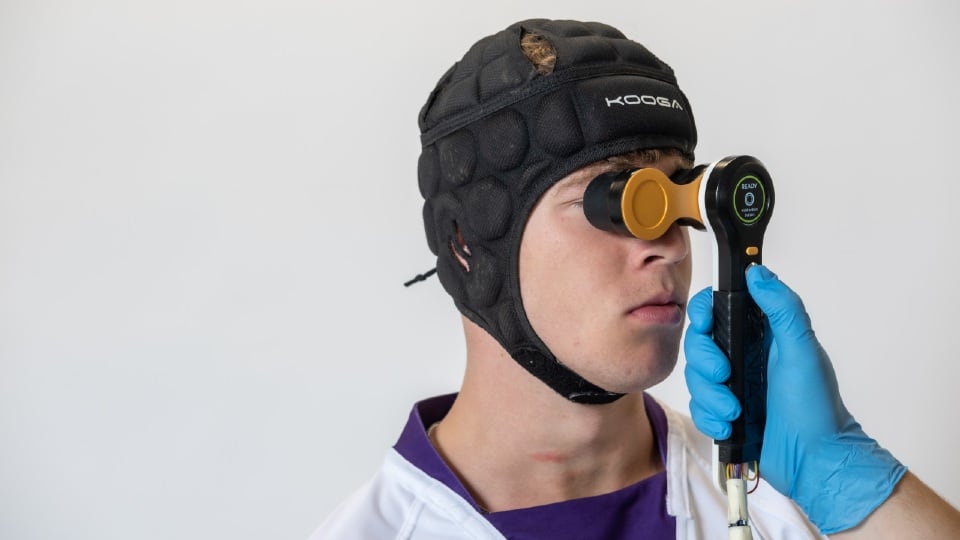 A hand-held concussion testing device being held up to a man's face