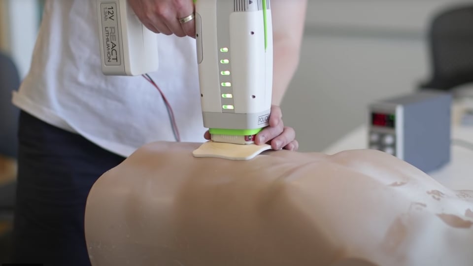 A hand-held electronic device being pressed into the torso of a medical dummy