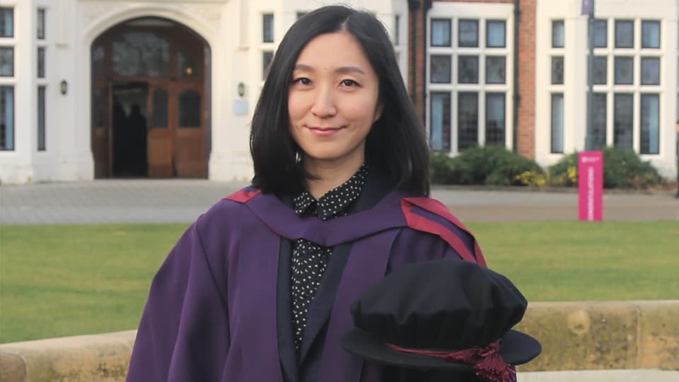 Yingzi Wang posing in the graduation gown on campus