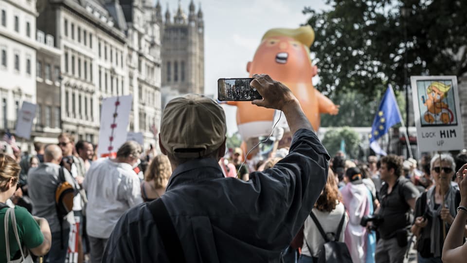 a man on the march taking a photo with his mobile of a giant trump look alike balloon