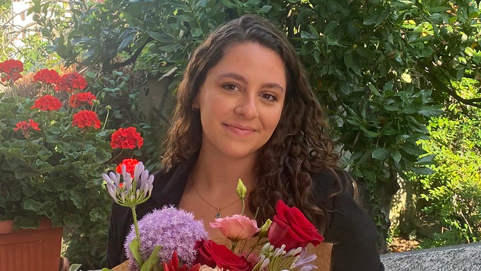 Costanza sitting outside with flowers around her