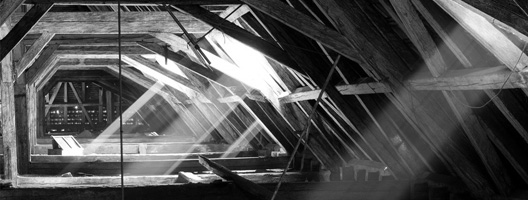 a room below a roof with wooden beams and sunlight and shadows
