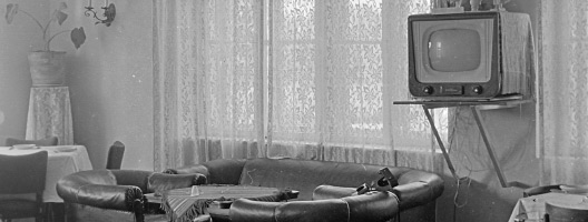 a living room with a TV on a wall bracket 1959