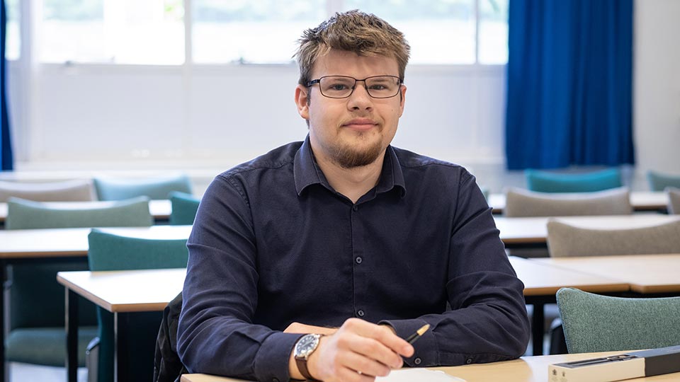 Caspar sat at a desk and holding a pen