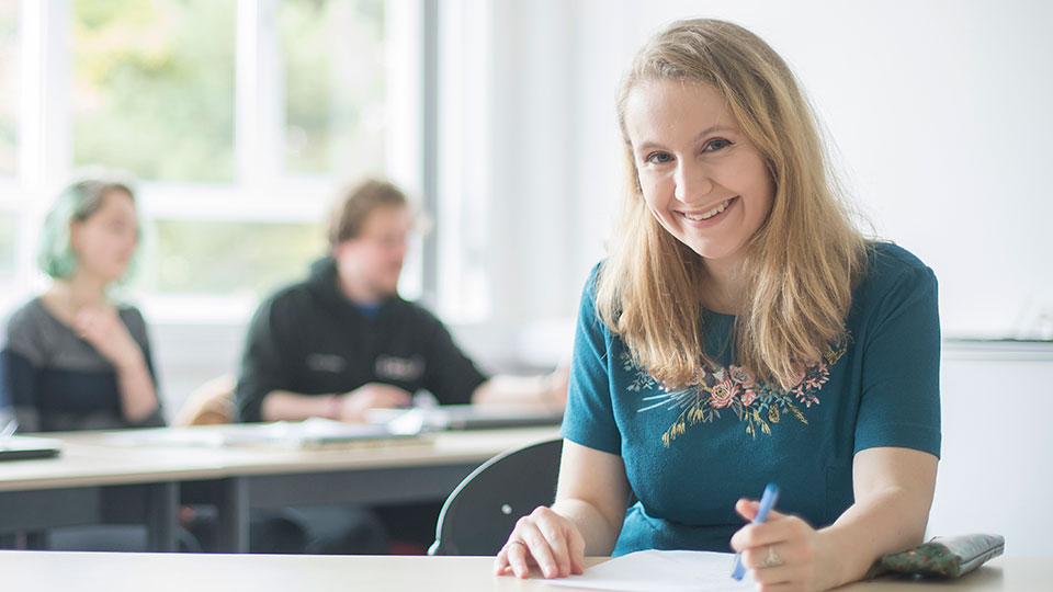 A student sat at a desk smiling at the camera