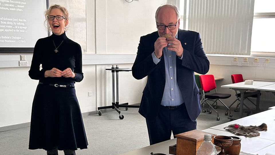 Dr Sara Read standing in a seminar room next to VC Nick Jennings who is eating a biscuit