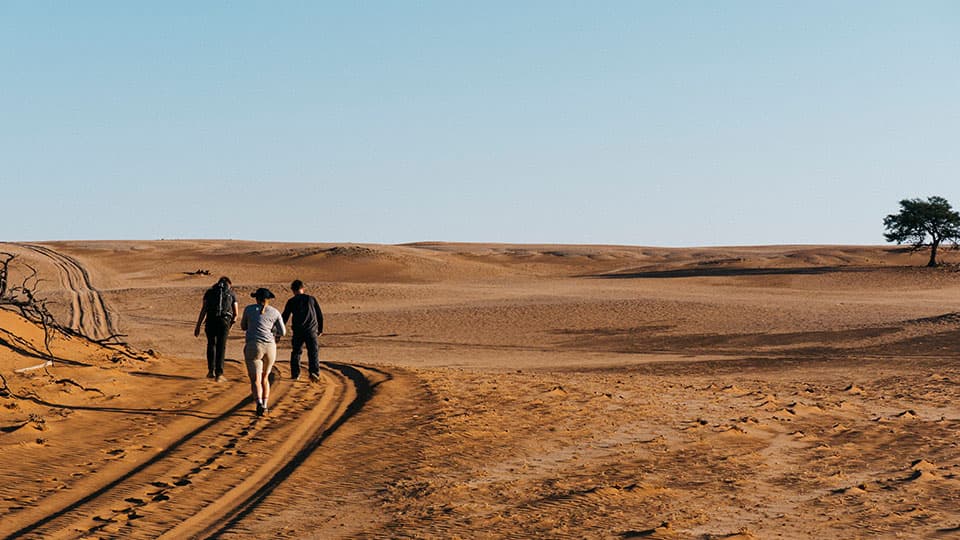 three people walking along a dirt track in the Namibia landscape