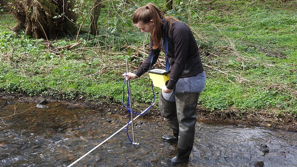 a student standing in a stream using measuring equipment