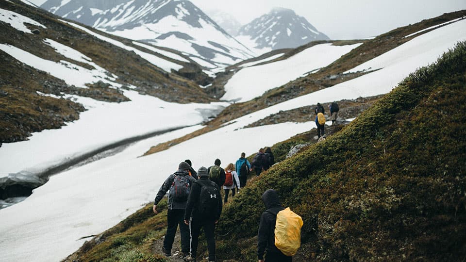 a group of people walking along a trail in a snowy landscape with distant mountains