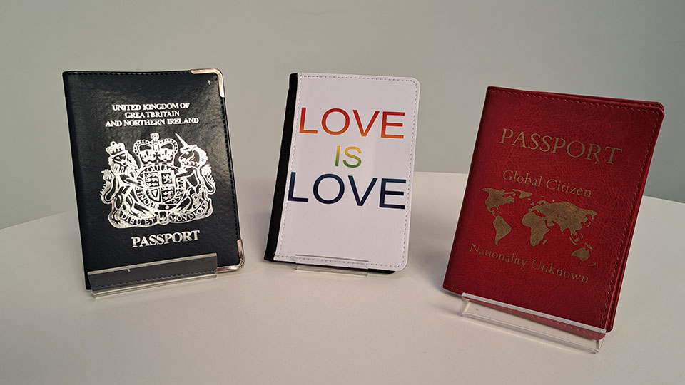 Two passports, one black, one red, either side of a wallet with the words 'Love is Love' printed on it