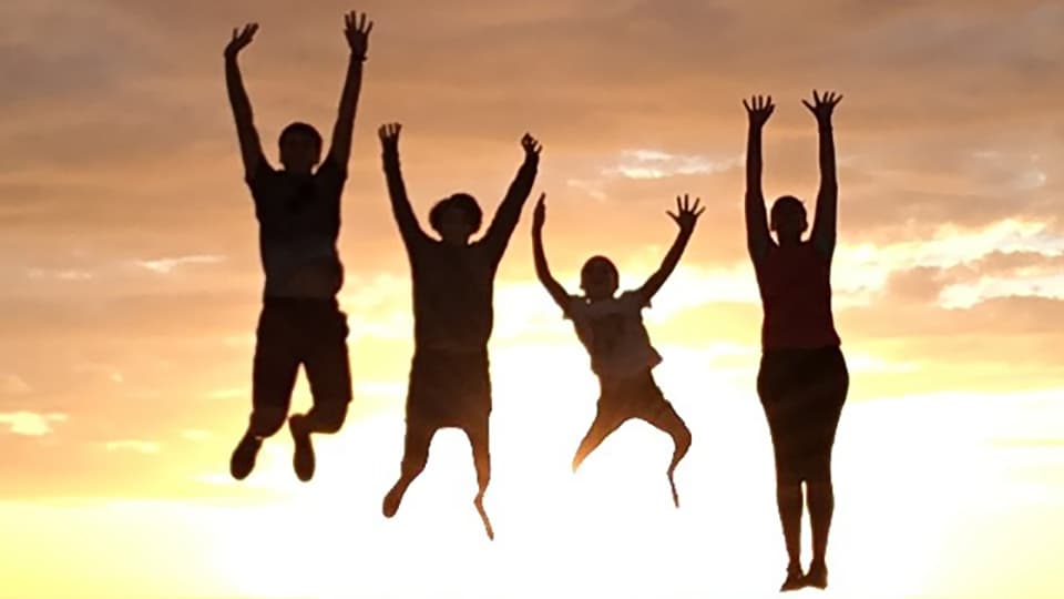 silhouettes of four people jumping against a sunset sky