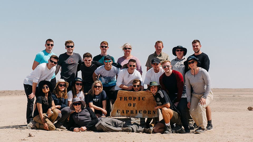a group photo in Namibia with a sign reading Tropic of Capricorn