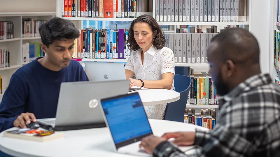 three people sitting at desks, working on laptops in the library