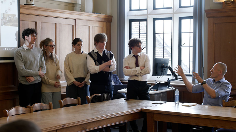 A group of students standing at the front of a large wood panelled room doing a presentation