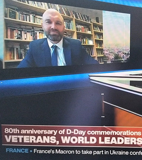 A screen capture of a news broadcast showing an interview with a man in a suit and tie