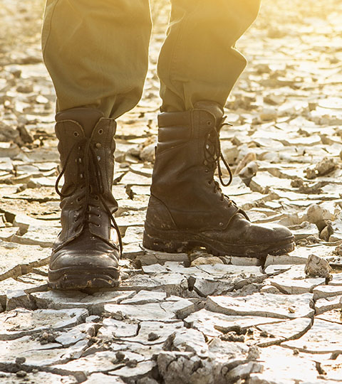 Close up of a soldier’s boots standing on cracked earth